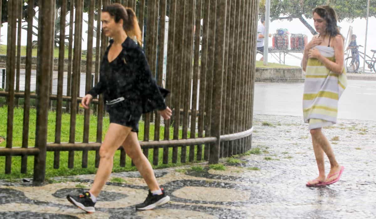 Na chuva, Cláudia Abreu é flagrada em Ipanema com a filha